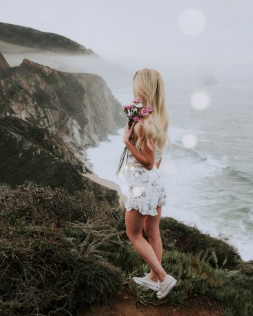 Whimsical Bohemian Girl with flowers at the big sun california coast cliffs